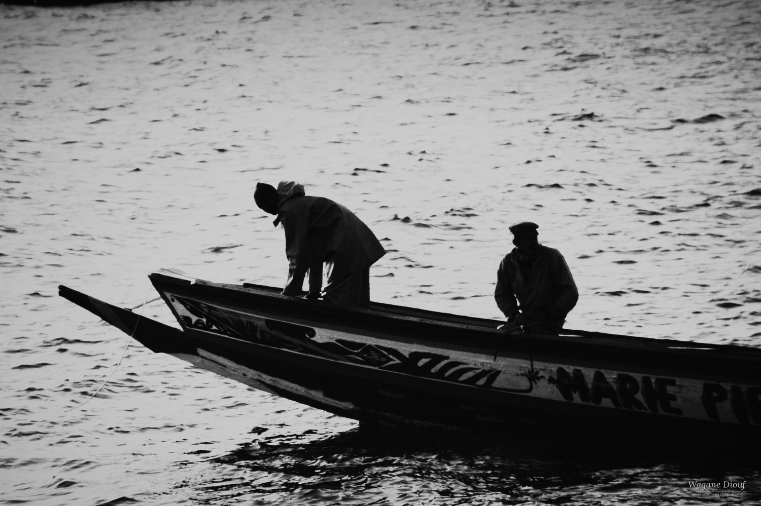 Two fishermen in silhouette on a pirogue over glittering water